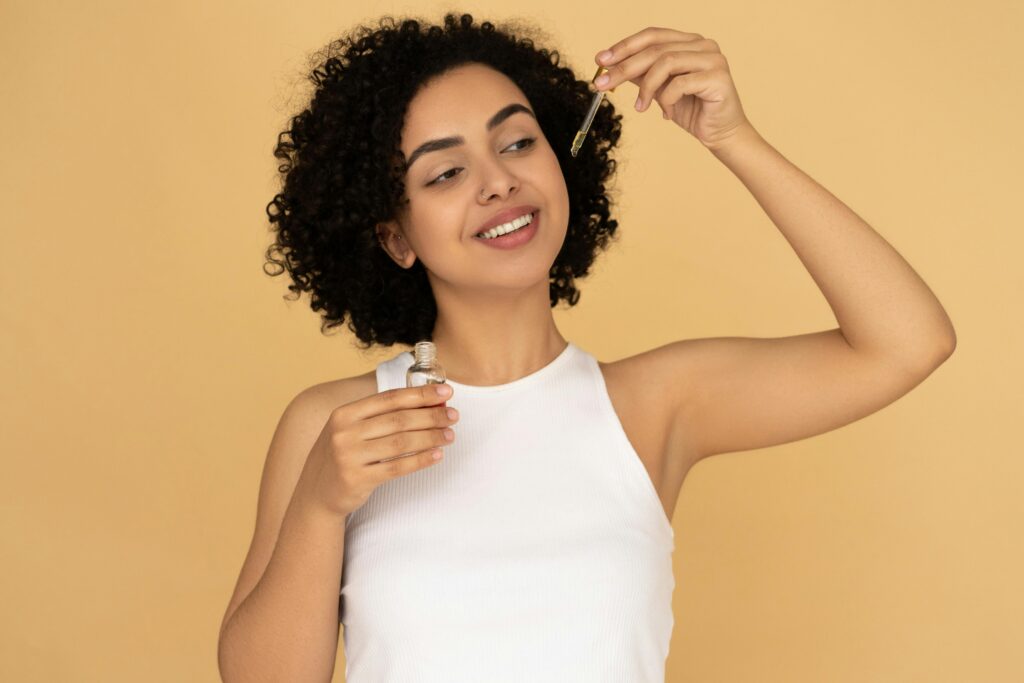 A smiling woman with curly hair applying essential oil for healthy skin care.
