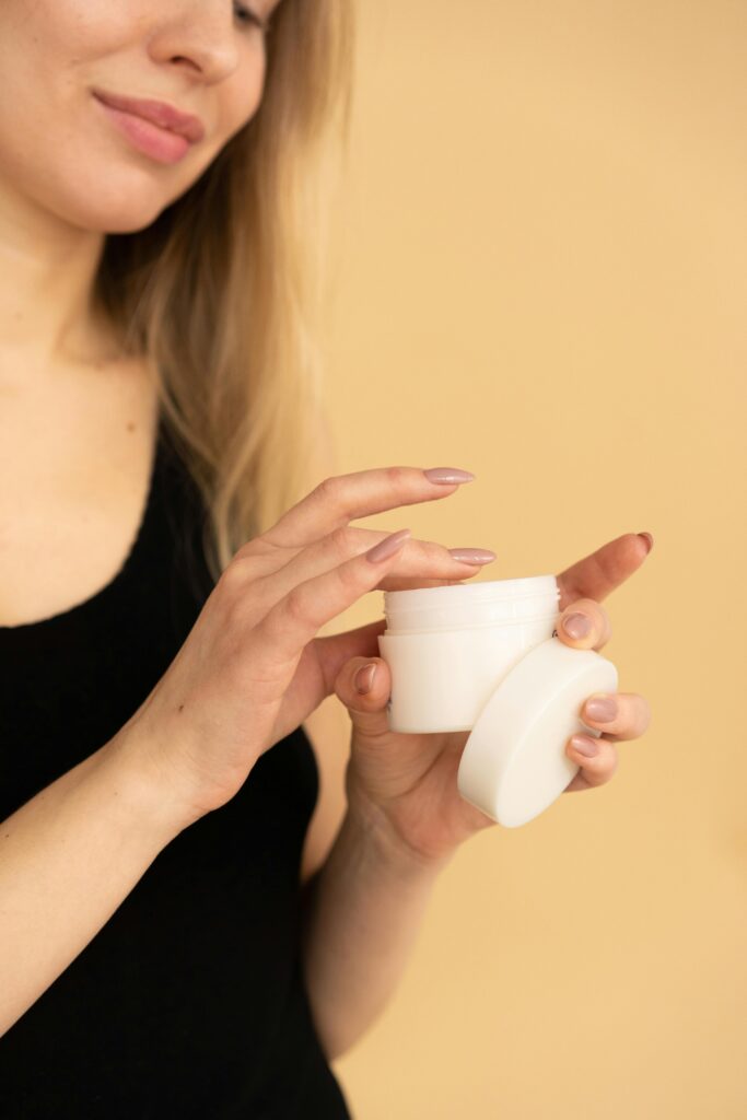 A woman applying moisturizer from a jar in a studio with a warm background.